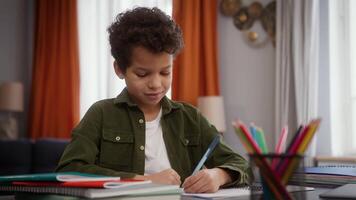 African American little child boy son kid pupil schoolboy sitting table home homework writing task write education study learning distant studying learn knowledge family smiling at camera happy smile video