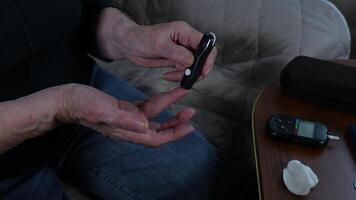 Close-up of senior's hands operating a portable glucometer while relaxing on living room sofa. Diabetes care and home health monitoring for active older adults video