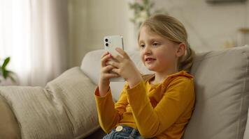 Little European girl user mobile phone smartphone cellphone online child chat networking browser internet electronic gadget device technology cyberspace daughter sofa connection website kid pupil home video