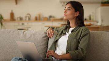 Serious concentrated Indian woman Arabian girl female working studying online at home typing laptop computer pensive looking away thinking ponder author write with pc think idea inspiration solution video
