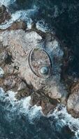 Top view of beautiful reef with waves and lighthouse. Clip. Single lighthouse on rocky ledge in blue sea on sunny day. Cinematic landscape of abandoned lighthouse on rocks in fantastic sea video