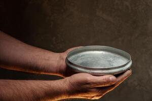 Male hands holding empty plate on dark background, lack of food, hunger concept. photo