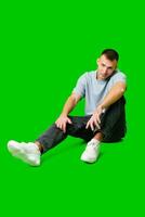 Casual Young Man Sitting on Floor in Comfortable Clothes With Green Background photo