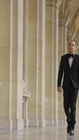 Man in black and white official suit walking in arcuate shaped hall. Action. Man walking outdoors by the building with columns. video