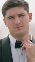 Young man in suit touching its bow tie outdoors. Action. Man wearing tuxedo standing in the field with fog. video