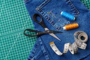 Sewing tools on a cutting mat with denim and thread spools in a craft workspace photo