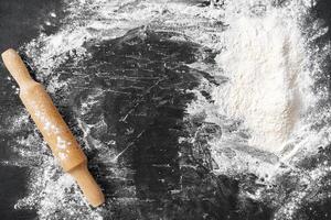 Scattered flour with rolling pin on black background photo