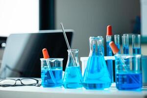 A table with a laptop, a few beakers and test tubes, and a blue liquid. The table is set up for a science experiment photo