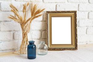 Vase with ears of wheat and photo frames against brick wall
