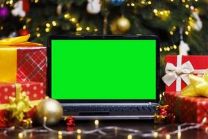 Laptop computer with green blank empty screen on table with gifts and garland photo