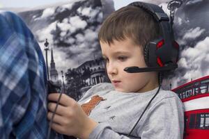 A boy sitting on a sofa in the room and listening to music or an e-learning class on his tablet computer with headphones. A child watching movie on digital tablet with headphones photo