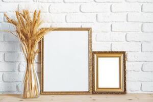 Vase with ears of wheat and photo frames against brick wall