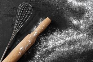 Scattered flour with rolling pin on black background photo