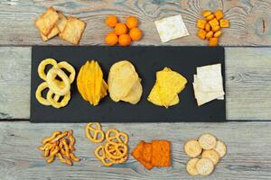 Mix of snacks . pretzels , crackers , chips and nachos on the table photo