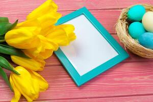 Easter concept. Wooden frame with easter eggs and tulips on colorful background photo