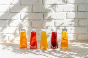 Row of glass bottles of different juices against white brick wall photo