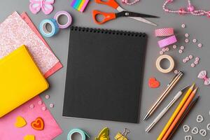 Crafting supplies arranged on a gray surface with a blank notebook, scissors, washi tape, and colorful embellishments photo