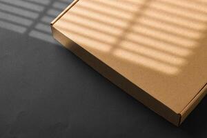 A cardboard box casting shadows on a dark surface in a striped light pattern photo