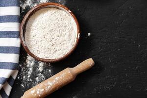 Scattered flour with rolling pin on black background photo