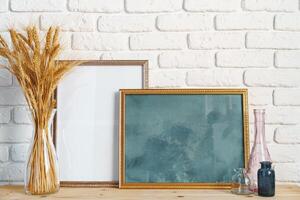 Vase with ears of wheat and photo frames against brick wall