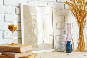 Vase with ears of wheat and photo frames against brick wall