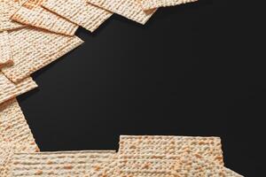 A photo of matzah or matza pieces on black background. Matzah for the Jewish Passover holidays. Place for text, copy space