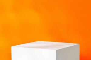 A white cube placed on a table against a vibrant orange wal photo