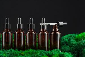 Dark glass bottles arranged in row on green moss against a black background photo