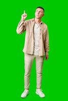 Young Man Pointing Upward While Smiling Against a Bright Green Background photo