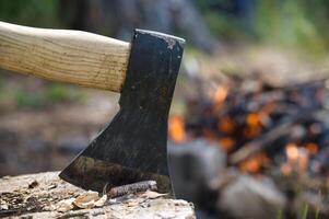 Close-up of an axe embedded in a log with a campfire burning in the background photo