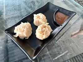 three dimsum on a black plate with sauce photo