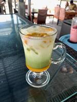 a glass of mango macchiato drink on the table. photo
