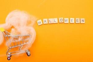 shopping cart with spider web and the inscription halloween on orange background. photo