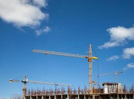 Construction site with multiple tall cranes working on building a high-rise structure under a clear blue sky photo