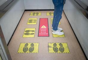 Woman standing on yellow footprint sign in lift or elevator and keep space for avoid spreading of virus disease in covid-19 pandemic. Social distancing puts space between people. photo