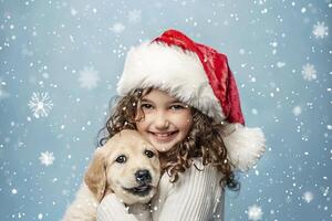 Little girl wearing a Santa Claus hat and holding a golden retriever puppy on a blue background. photo