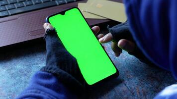 A man in a hoodie is using a smartphone with a green screen video