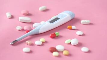 A thermometer and a pile of pills on a pink background video