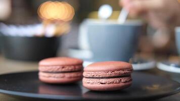 Two macarons on a black plate with coffee cups in the background video