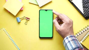 A man's hand touching a smartphone with a green screen on a yellow background video