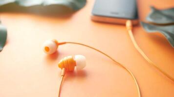 A pair of earphones and a smartphone on an orange background video