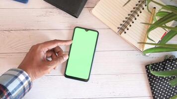 A man using a smartphone with a green screen on a wooden table video