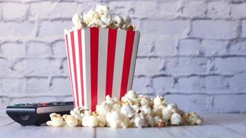 A red and white striped popcorn bucket with a remote control video