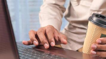A man holding a coffee cup and using a laptop video