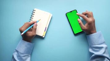 Hands writing in notebook with green screen and smartphone on blue background video