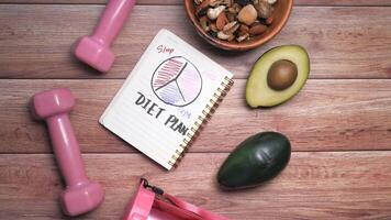 mancuernas, palta, y un cuaderno con el palabra dieta plan video