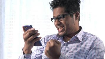 A man in glasses is smiling while holding a cell phone video