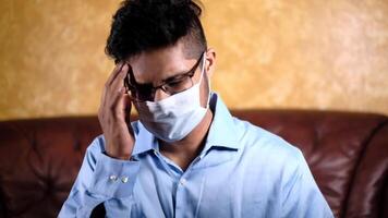 A man wearing a face mask and glasses sits on a couch video