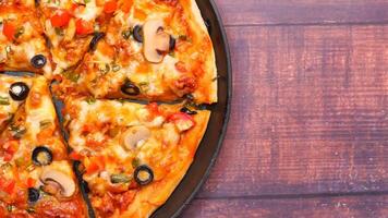 A pizza with cheese, olives, mushrooms and tomatoes on a wooden table video