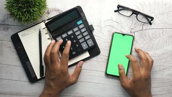 A woman's hands using a calculator and a smartphone to calculate the cost of a car video